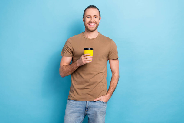 Photo of positive good mood man wear beige t-shirt smiling drinking hot beverage isolated blue color background. - Photo, Image