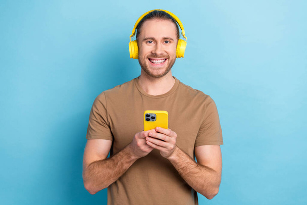 Photo of positive cheerful guy dressed beige t-shirt headphones listening music modern gadget isolated blue color background. - Photo, image