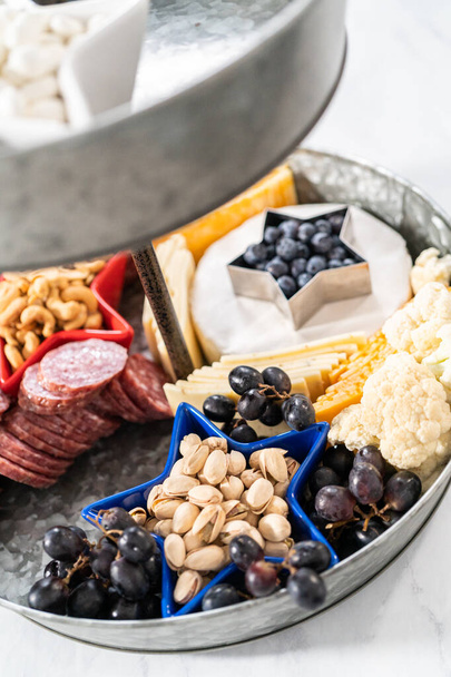 4 июля на двухъярусной доске из металла, наполненной сыром, крекерами, салями и свежими фруктами - Фото, изображение