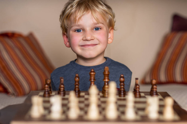 Small child 5 years old playing a game of chess on large chess board. Chess board on table in front of the boy thinking of next move, tournament - Foto, Bild
