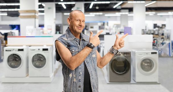 Bald man in a denim vest pointing at an appliance store - Fotoğraf, Görsel