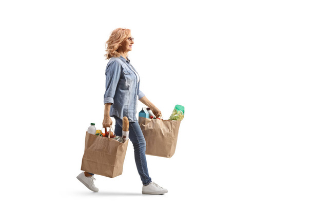 Full length profile shot of a mature woman carrying grocery bags and walking isolated on white background - Photo, image