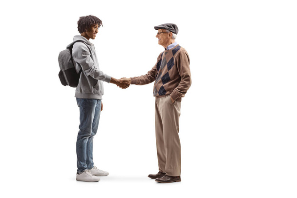 Full length profile shot of an african american male student and a caucasian senior man shaking hands isolated on white background - Foto, afbeelding