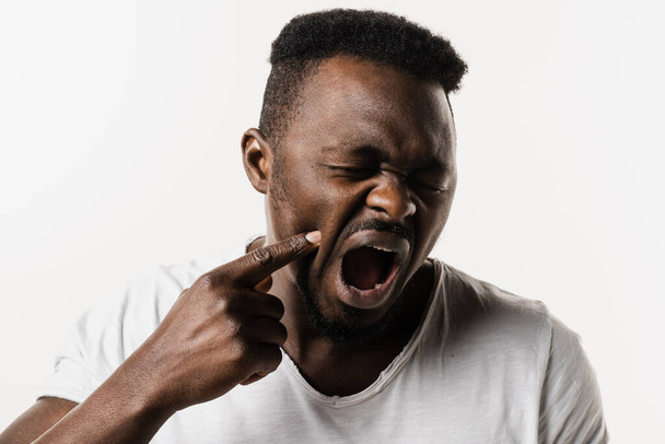 African man with tooth decay, infection or injury to the tooth or gums on white background. African american man is touching cheek and feeling toothache pain and discomfort of tooth - Fotografie, Obrázek