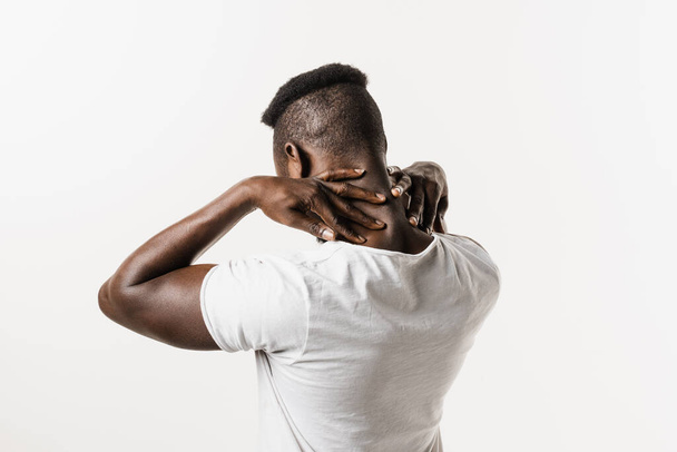 Afrikalı adam, beyaz arka planda omurga ve boyun ağrısı hissediyor. Servikal omurga osteokondrosis Afro-Amerikan erkeklerinin radikal sendromlarıdır. - Fotoğraf, Görsel