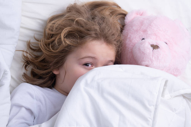 Morning awakening little child with toy teddy bear in bed. Kid wakes up in the bedroom - 写真・画像
