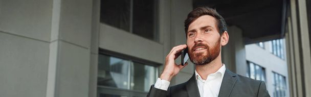 Smiling businessman in suit with coffee talking phone near office building. Business concept - Photo, Image