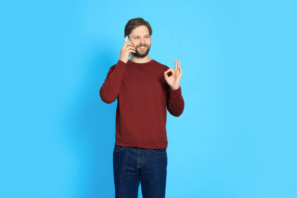 Man talking on smartphone against light blue background - Фото, изображение