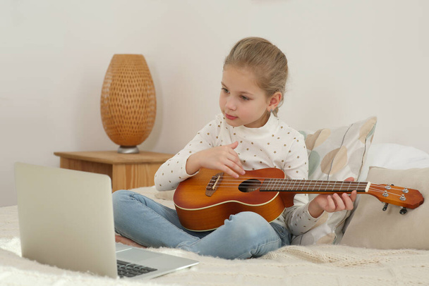 Little girl learning to play ukulele with online music course at home. Time for hobby - 写真・画像