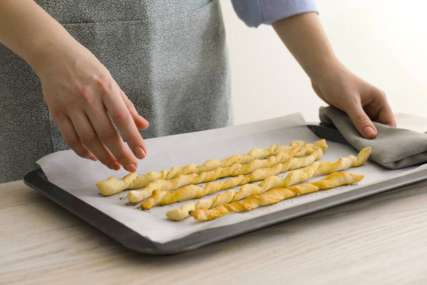 Woman near baking sheet with homemade breadsticks at white wooden table, closeup. Cooking traditional grissini - Photo, image