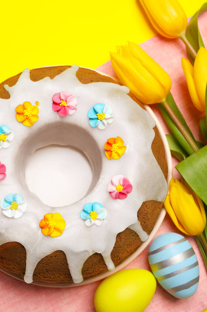 Delicious Easter cake decorated with sprinkles near beautiful tulips and painted eggs on yellow background, flat lay - Photo, Image