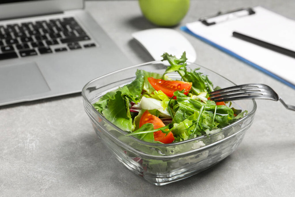 Fresh vegetable salad, laptop and fork on light grey table at workplace, closeup. Business lunch - Фото, зображення