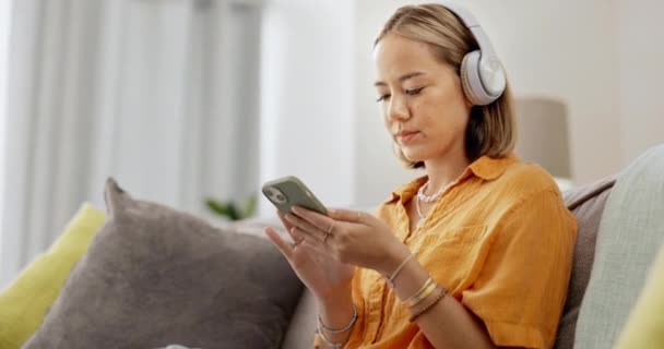 Dance, music and search for woman with headphones and phone for streaming, playlist or song on sofa. Radio, dancing and asian girl chilling, happy and and smile in living room with podcast selection. - Filmagem, Vídeo