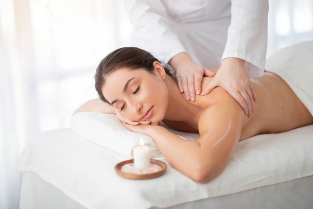 Wellness-Massage. Schöne Inderin bekommt Körperbehandlung durch einen professionellen Masseur im Salon, entspannte Hindu-Frau genießt Schönheitsbehandlungen, liegt mit geschlossenen Augen auf dem Tisch, Nahaufnahme - Foto, Bild