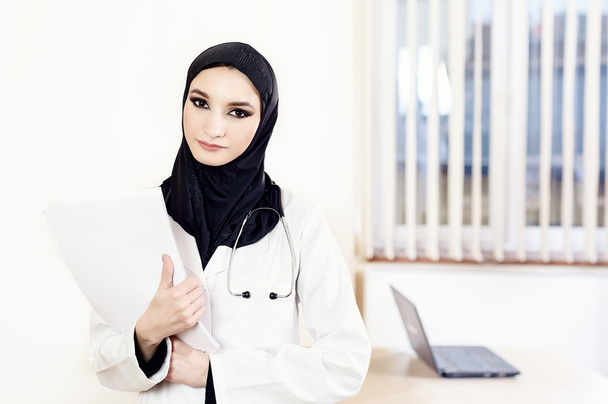 Μουσουλμανική γυναίκα γιατρό μόνιμης και κρατώντας ιατρικά αρχεία - Φωτογραφία, εικόνα