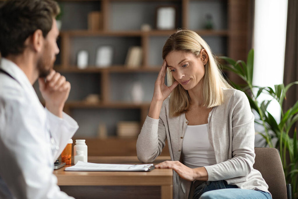zestresowana kobieta patrząc na jej wyniki kontroli podczas spotkania z lekarzem w biurze, zamyślona kobieta dotykająca głowy pacjenta, podczas gdy terapeuta mężczyzna wyjaśniając szczegóły leczenia, selektywne skupienie - Zdjęcie, obraz