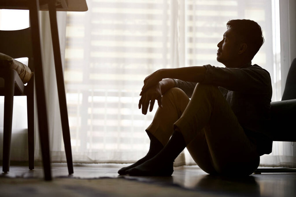 Homme asiatique déprimé et frustré assis sur le plancher du salon, chambre noire, souffrant d'échec de la vie, manque d'énergie, pas de passion, anxiété. silhouette image - Photo, image