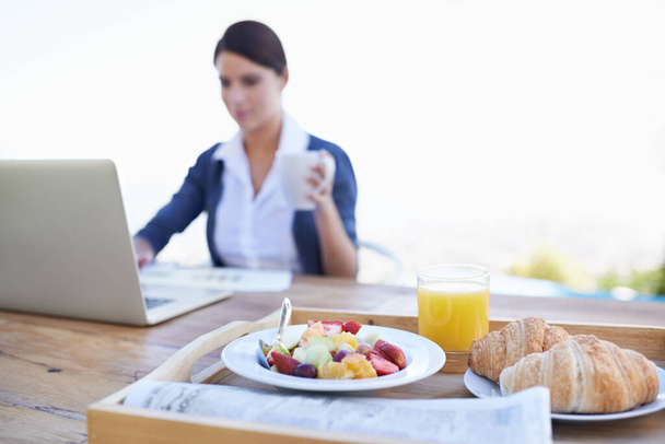 Checking her e-mails before breakfast. An attractive young woman working on her laptop with her breakfast in focus - Fotoğraf, Görsel