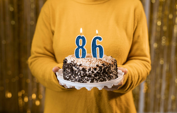 Žena drží slavnostní dort s číslem 86 svíčky při oslavě narozeninové oslavy. Koncept lidí na oslavu narozenin. Pohled zblízka - Fotografie, Obrázek