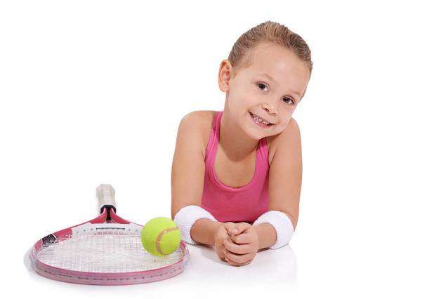 Elle est devenue une star du tennis. Portrait studio d'une jolie petite fille en tenue de tennis couchée à côté de sa raquette de tennis et de sa balle - Photo, image
