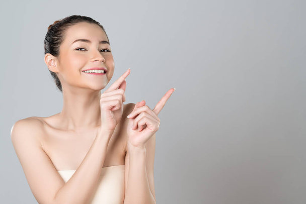 Glamorous beautiful woman with perfect makeup clean skin pointing finger in copyspace isolated background. Promotion indicated by hand gesture concept for skincare product advertisement. - 写真・画像
