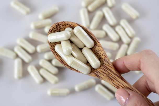 Beige koude en griepcapsules in een houten lepel. Supplementen en medicijnen. Close-up, bovenaanzicht - Foto, afbeelding