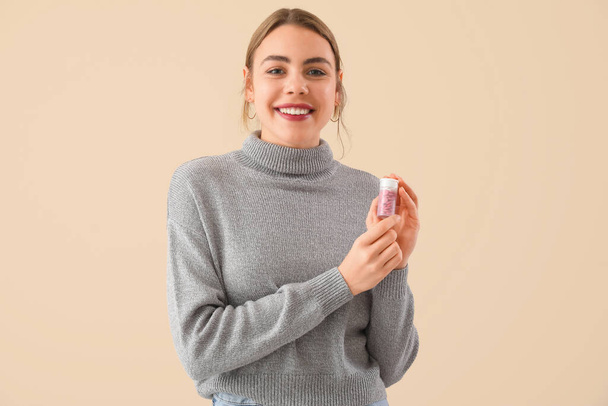 Beautiful young woman with bottle of vitamin supplements on beige background - Fotografie, Obrázek