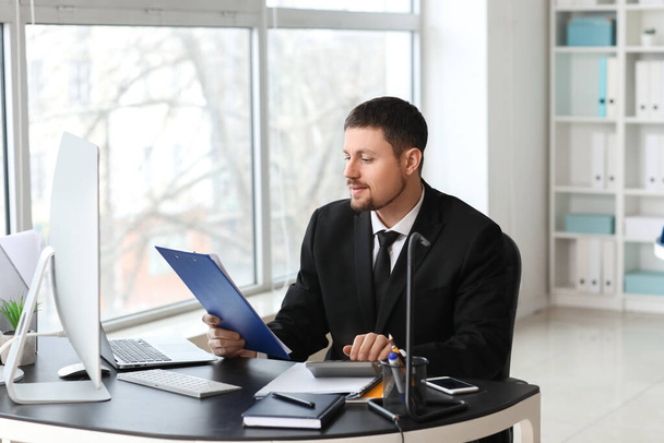 Мужчина бухгалтер, работающий с документами и калькулятором за столом в офисе - Фото, изображение