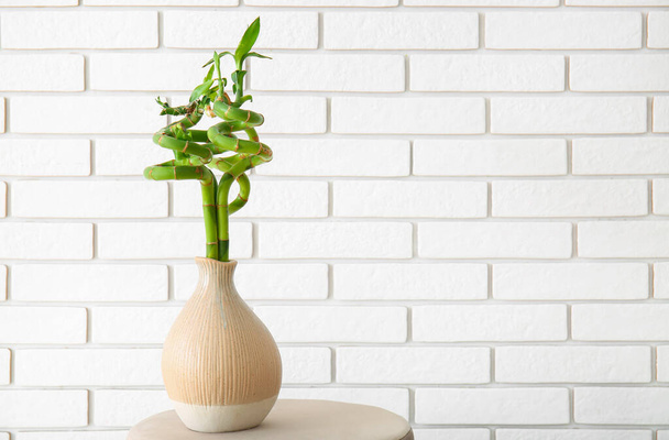 Vase with bamboo plant on table near brick wall - 写真・画像