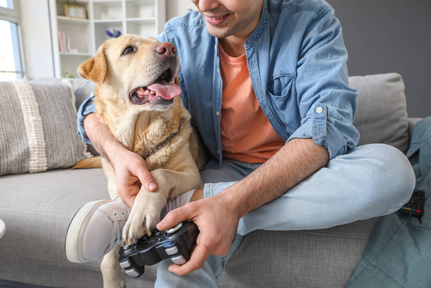 Young man with cute Labrador dog playing video game at home, closeup - 写真・画像