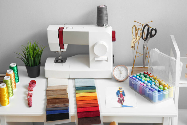 Lugar de trabajo del sastre con máquina de coser, muestras de tela y carretes de rosca en el taller - Foto, imagen
