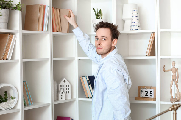 Young man taking book from shelf at home - Valokuva, kuva