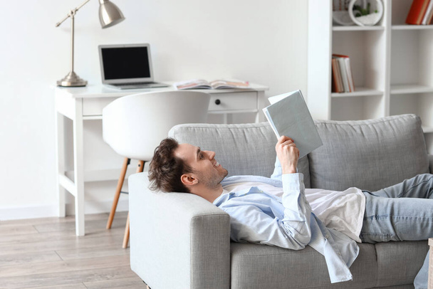 Young man reading book on sofa at home - Foto, Imagem