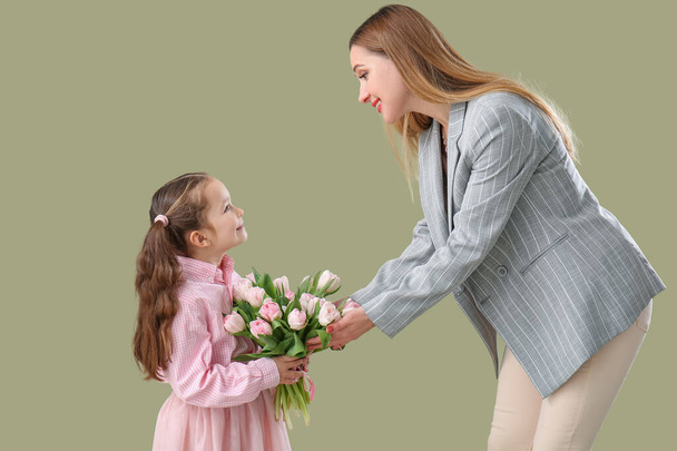 Cute little girl greeting her mother with tulips on green background - Φωτογραφία, εικόνα