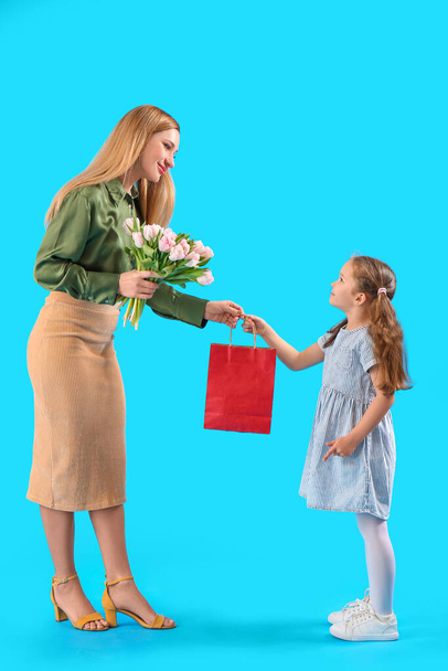 Cute little girl greeting her mother with tulips and bag on blue background - Foto, Bild