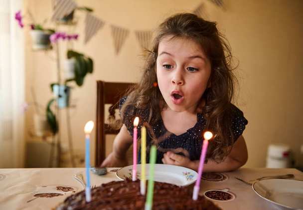 Lovely little child, cute baby girl with beautiful long curly hair, wearing elegant dress, blowing out candles on her birthday cake - Foto, imagen