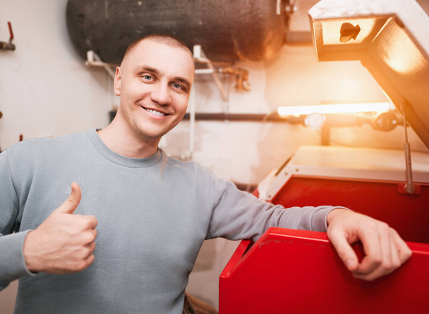 Industrial system engineer shows off his smile while fixing the heating system. Caucasian engineer recommends to use sustainable heating systems - Photo, Image