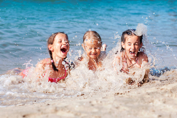 Happy Children Having fun Playing with Sea Waves on Sandy Beach. Funny Kids Swiming and Splashing. Travel Holiday concept - Zdjęcie, obraz