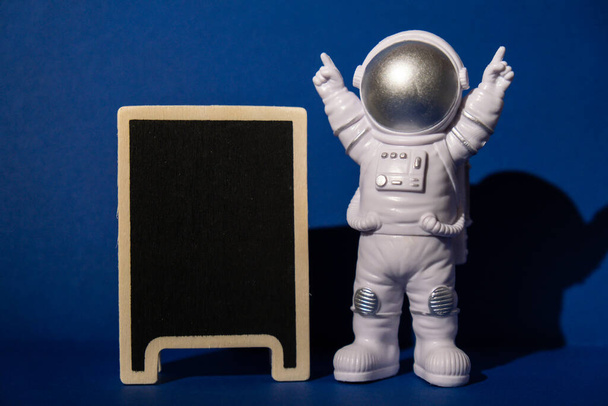 Plastic toy astronaut with blackboard template mock up for your text on colorful blue background Copy space. Concept of out of earth travel, private spaceman commercial flights. Space missions and - Foto, afbeelding