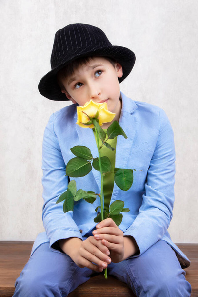 Portré egy fiúról kalapban és öltönyben egy rózsával. Gyermek virággal anyák napjára vagy ünnepére. Elegáns vicces ember egy virággal ajándékba.. - Fotó, kép