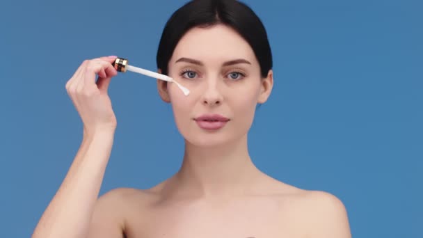 close-up of an attractive European young woman applies a face care serum to her cheek from a pipette. Facial serum advertisement - Video, Çekim