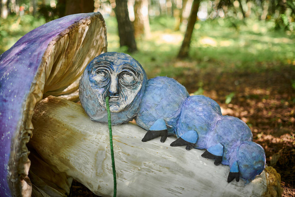 Hookah palenie gąsienica z Alicji Wonderland obiekt sztuki na zewnątrz wystawa sztuki w zielonym lesie, surrealizm atmosferyczny. Palenie gąsienica leżące na duży grzyb, baśniowy obiekt sztuki - Zdjęcie, obraz