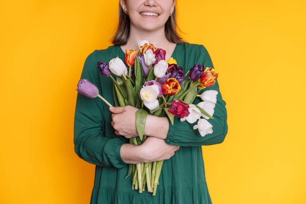 Lady in green dress holding bouquet of tulips in front of yellow background. - Foto, immagini