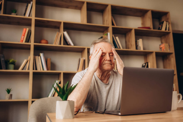 Müder Senior mit Kopfschmerzen in der Bibliothek nach der Benutzung des Computers - Foto, Bild