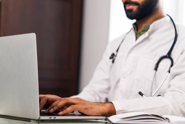 Portrait of indian man doctor talking to online patient on laptop online consultation. - Фото, изображение
