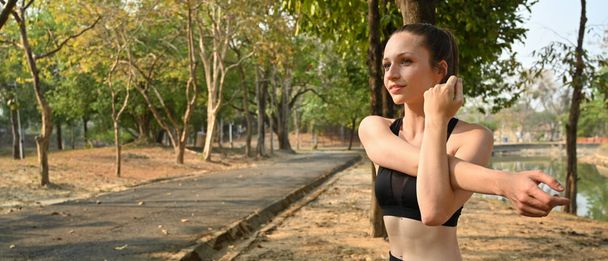 Gorgeous sporty caucasian woman in sportswear stretching body before running in the park. Healthy lifestyle concept. - Foto, afbeelding
