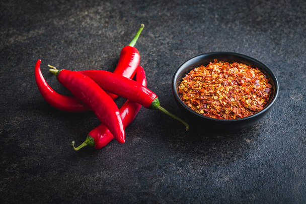 Dry chili pepper flakes. Crushed red peppers in bowl on the black table. - Foto, immagini