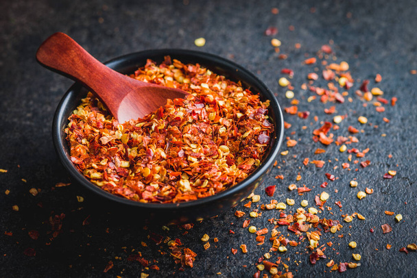 Dry chili pepper flakes. Crushed red peppers in bowl on the black table. - Фото, зображення