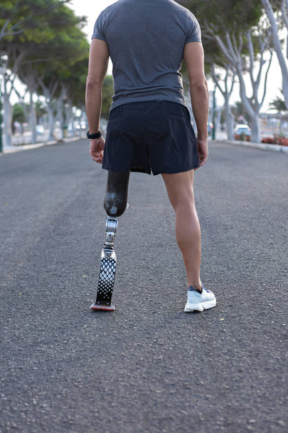 Achteraanzicht van gewas anonieme mannelijke atleet in sportkleding met kunstmatig lemmet been staan op straat en voor te bereiden op het lopen in de stad - Foto, afbeelding