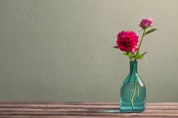 pink peonies in glass vase on green background - Фото, изображение